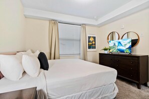 Ein Schlafzimmer mit Bett, Kommode, Fernseher und einem Fenster mit Vorhängen.