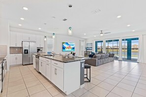 Cozinha espaçosa com armários brancos, uma ilha grande e um espaço de jantar com sofá cinzento.