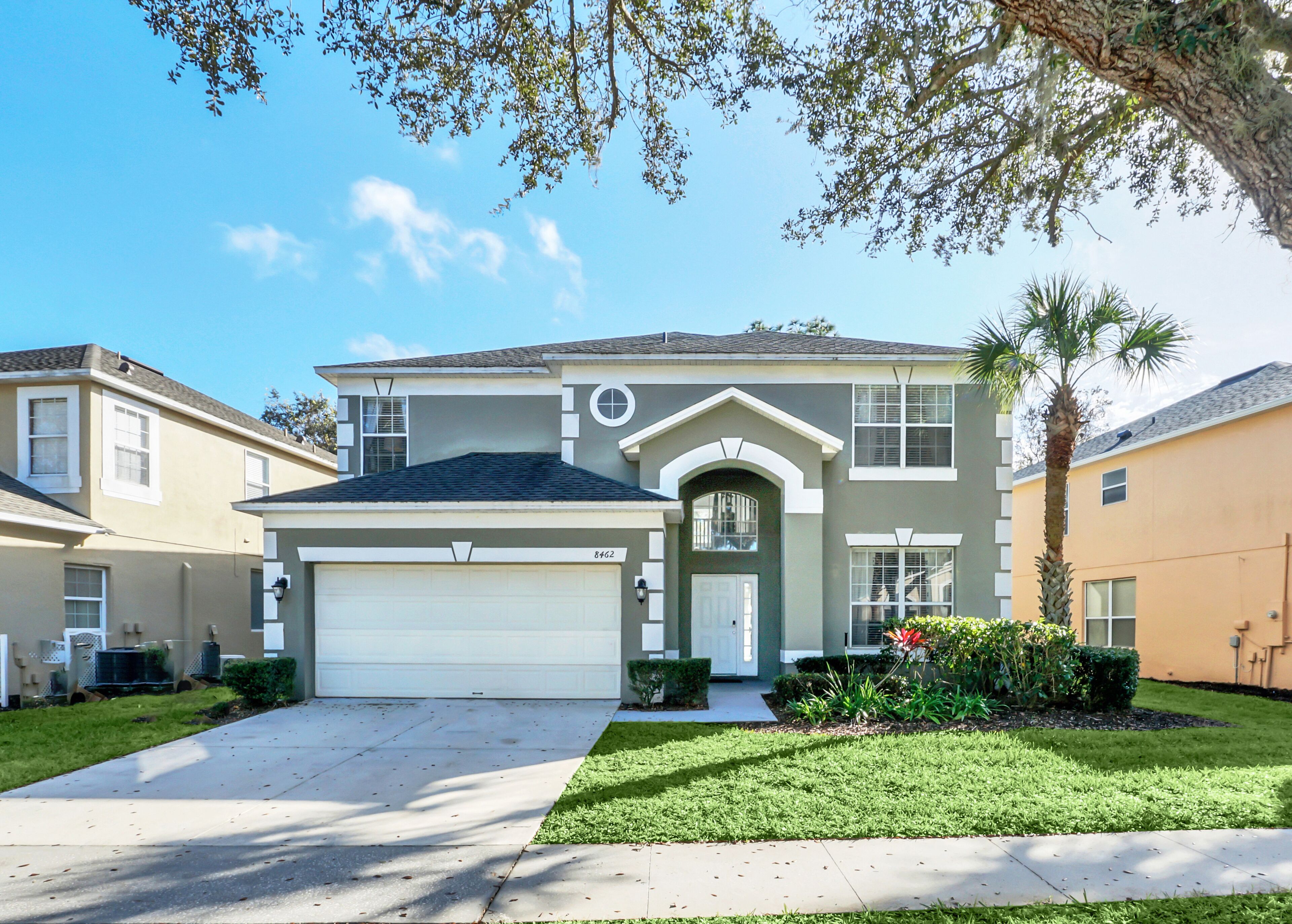 A two-story house with a garage, a front yard with a palm tree, and a well-maintained lawn.