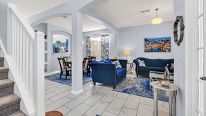 Un grand espace de vie comprenant un canapé bleu, une table à manger avec des chaises, et une cuisine en arrière-plan.