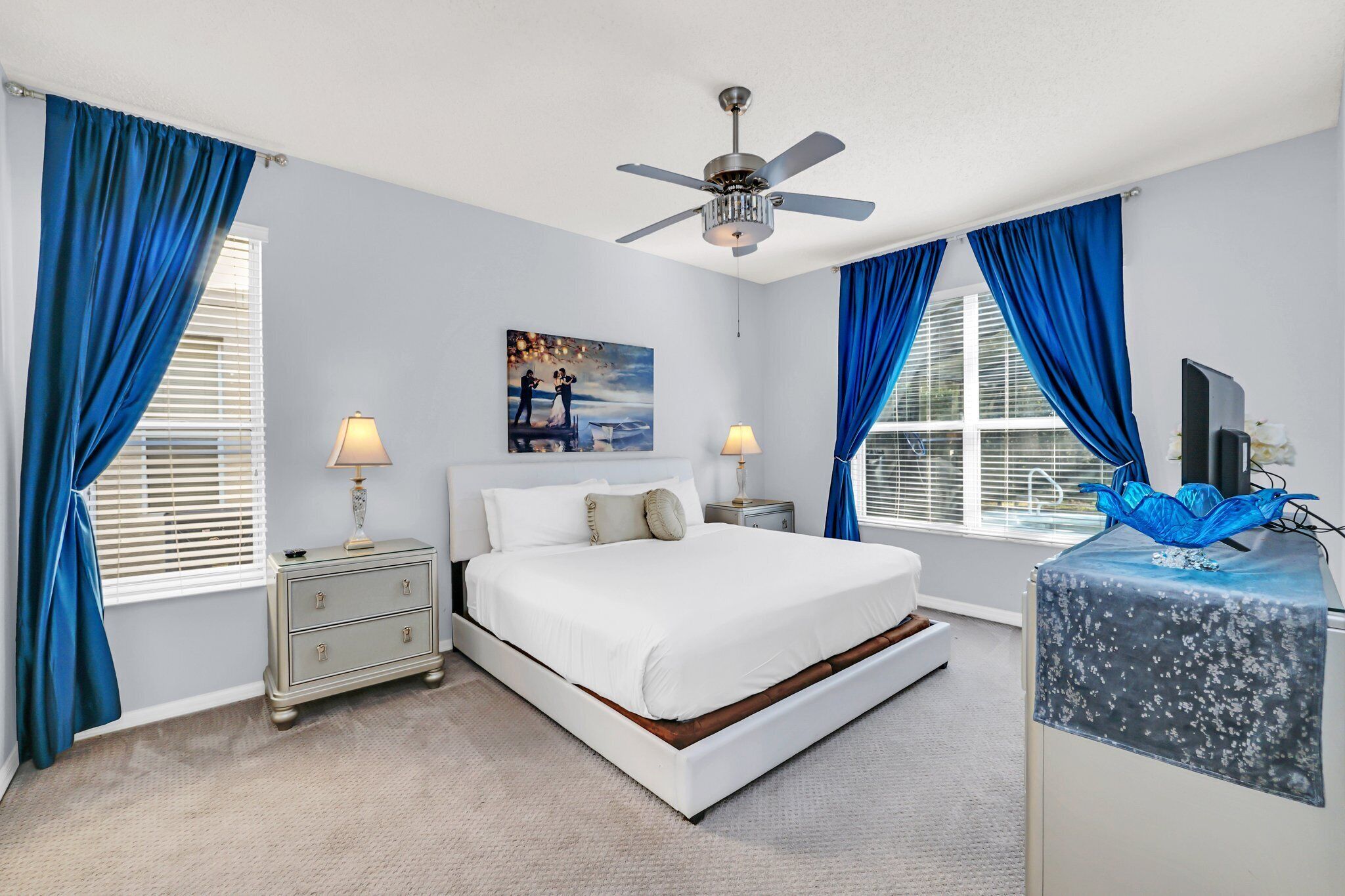 A bedroom with a bed, nightstands, a ceiling fan, and a TV on a stand.