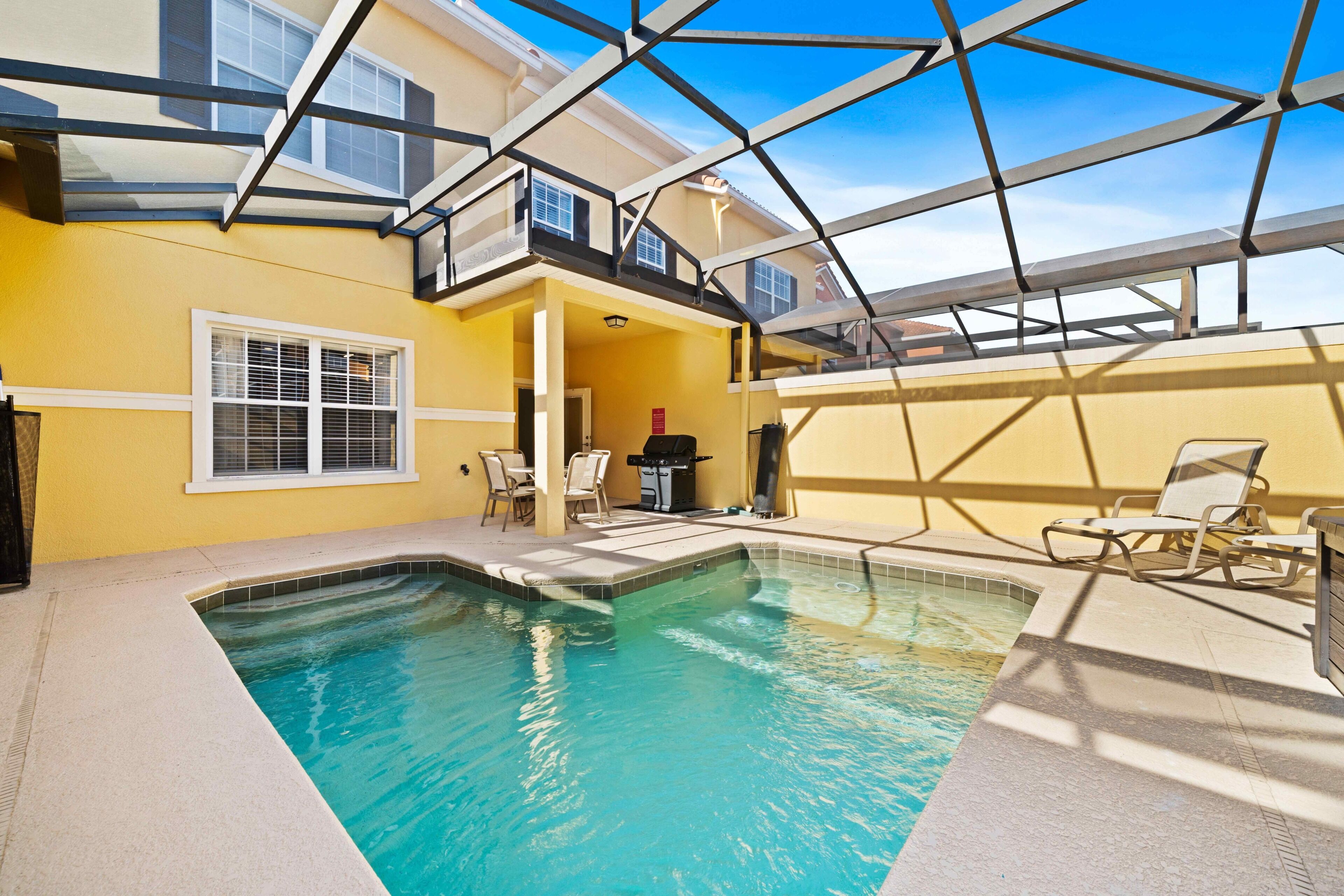 A swimming pool with a glass ceiling, yellow walls, and a patio area with chairs.