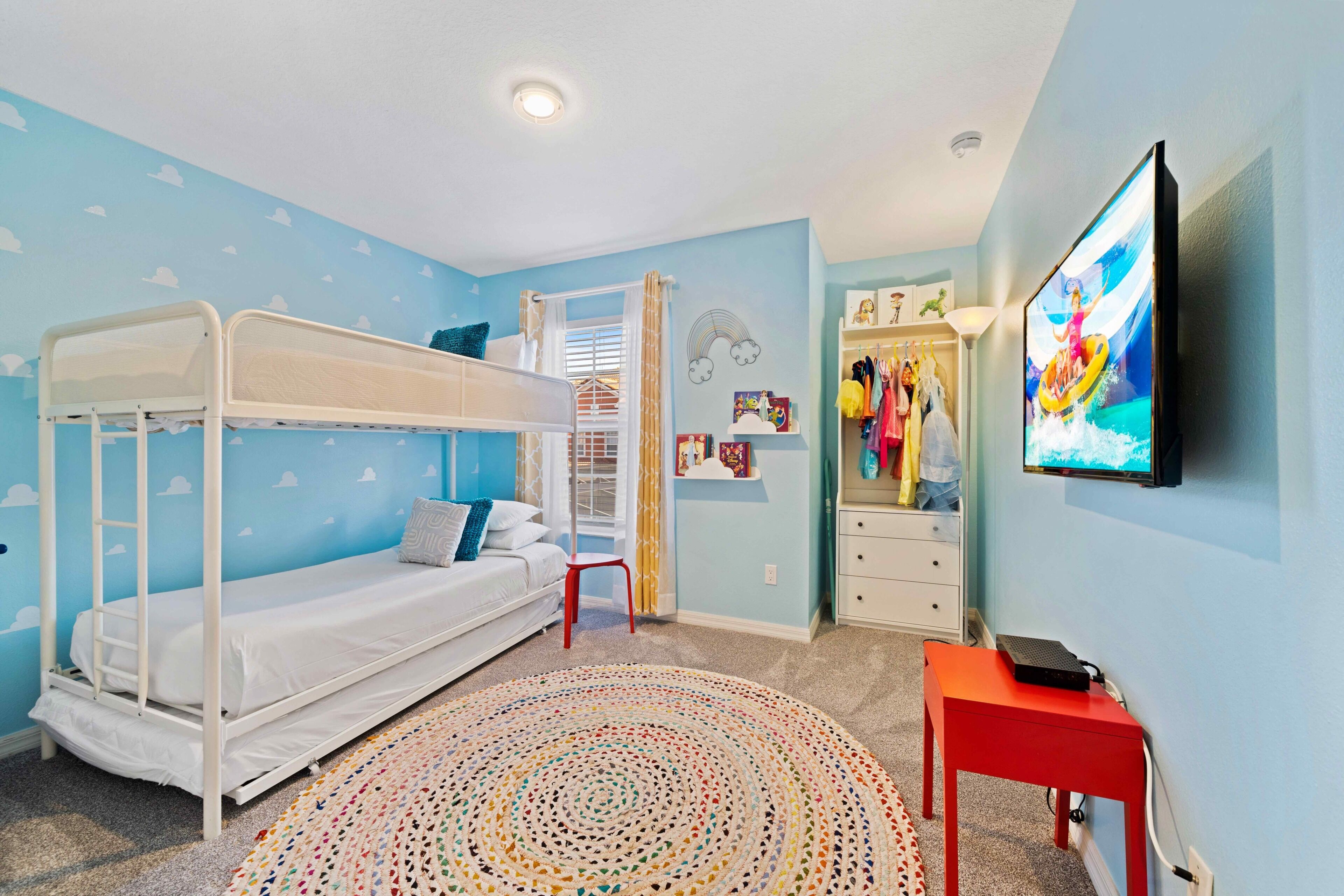 A bedroom with bunk beds, a TV, a red table, and a colorful rug.