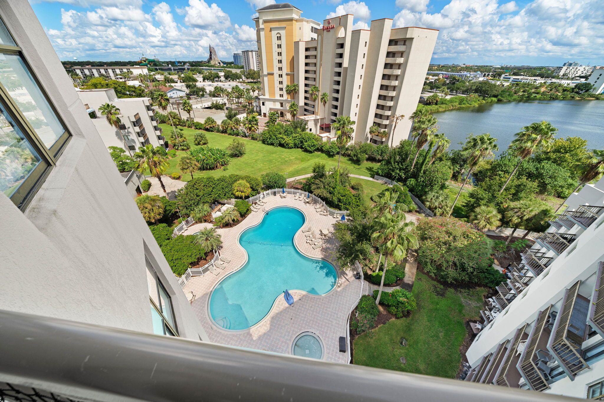 A hotel with a pool, surrounded by greenery and a view of a body of water.