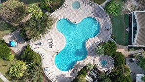 Vue aérienne d’une piscine en forme de cœur, entourée de chaises longues et d’une petite zone aménagée en terrasse.