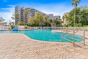 Une piscine dotée d’une terrasse carrelée, entourée d’une clôture blanche et de palmiers.
