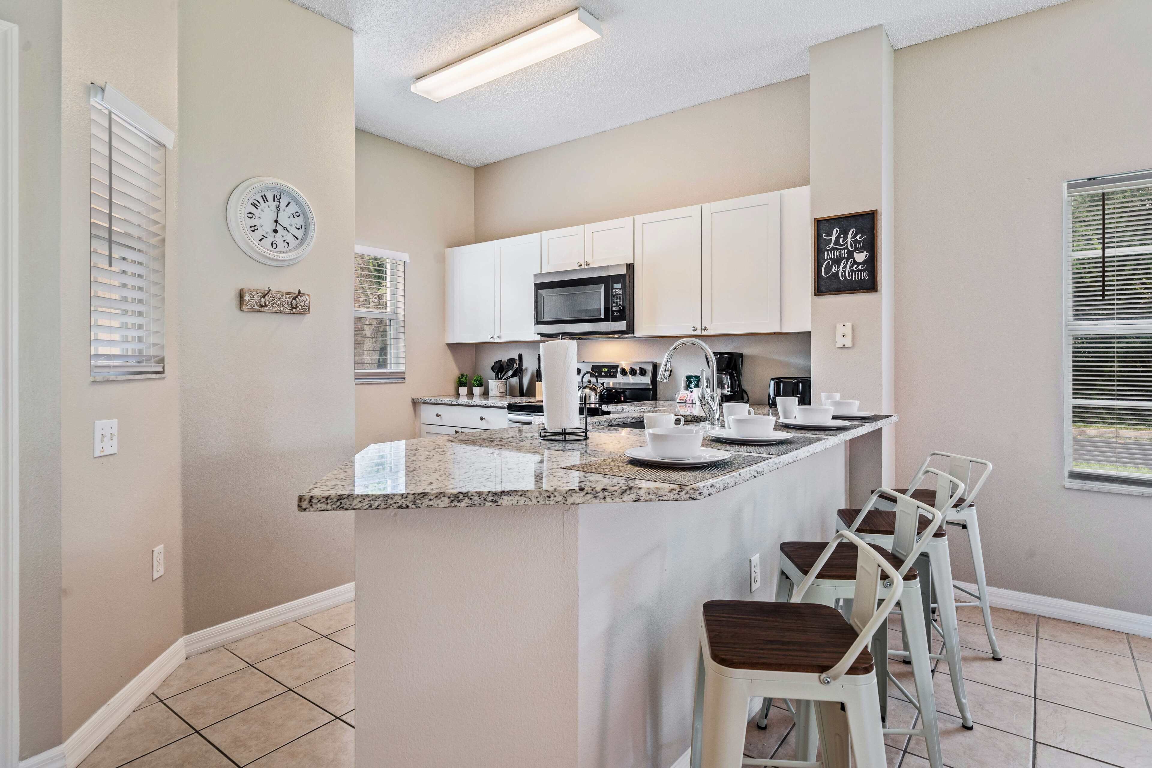A modern kitchen with white cabinets, a granite countertop, a microwave, and a coffee station.