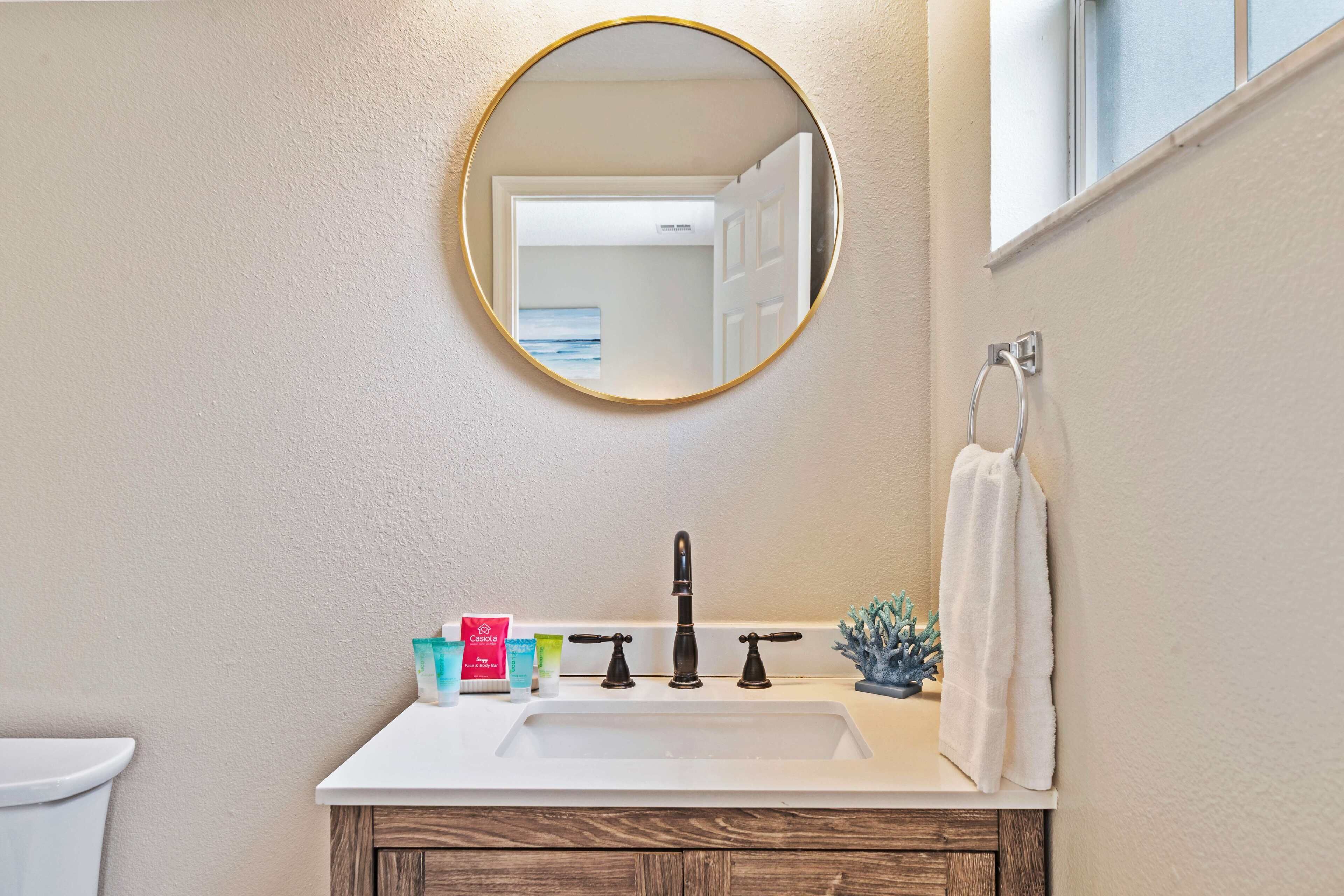 Une salle de bain avec un lavabo blanc, un miroir rond et un porte-serviettes.