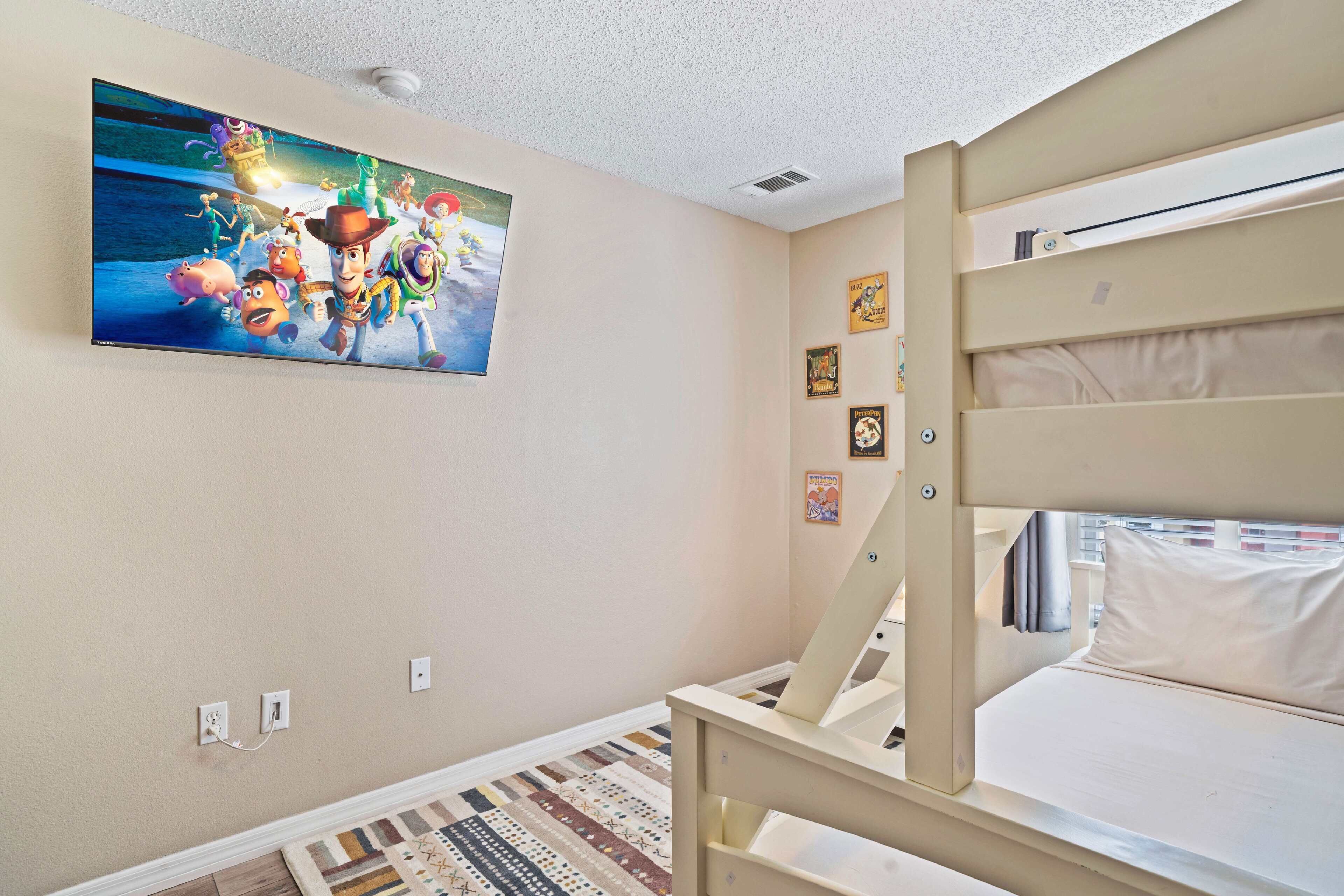 Ein Schlafzimmer mit einem Etagenbett, einem an der Wand befestigten Fernseher, der einen Film zeigt, und einem gemusterten Teppich.