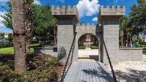 A stone archway with a wooden walkway leading through it, surrounded by greenery and palm trees. - 2533 Renshaw Street (Kissimmee)