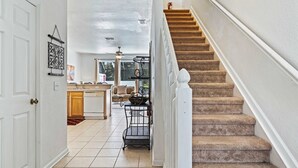 A staircase leading to a second floor, a kitchen area with a dining table, and a hallway with a white door. - 2533 Renshaw Street (Kissimmee)