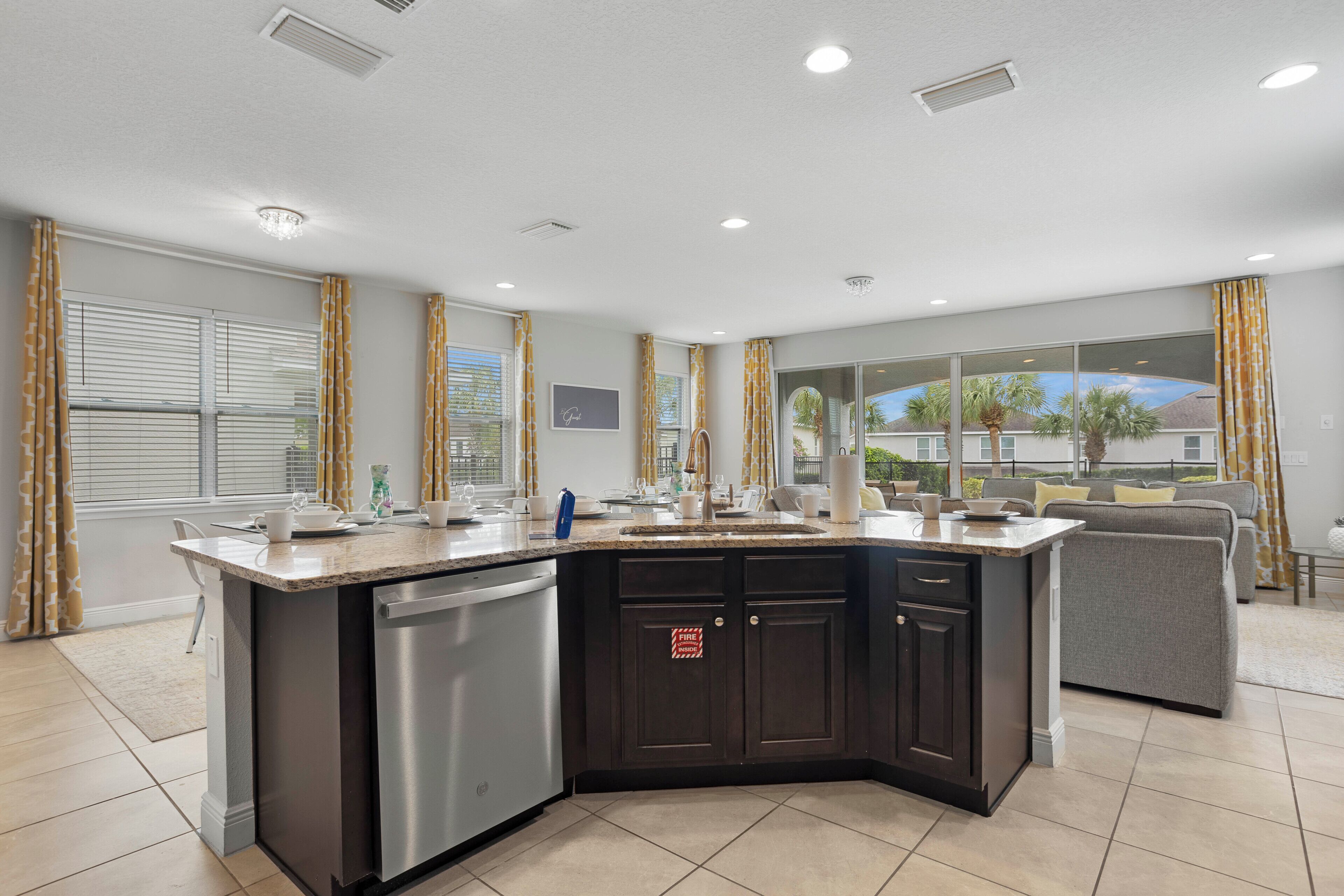 A modern kitchen with a large island, dark cabinetry, and a view of the outdoors.
