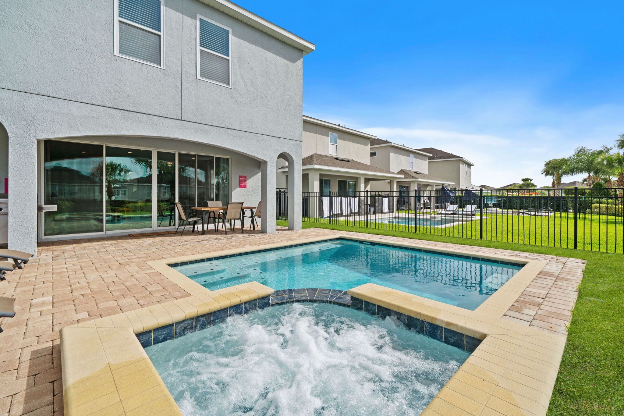 A residential building with a swimming pool, patio with chairs, and a fenced yard.