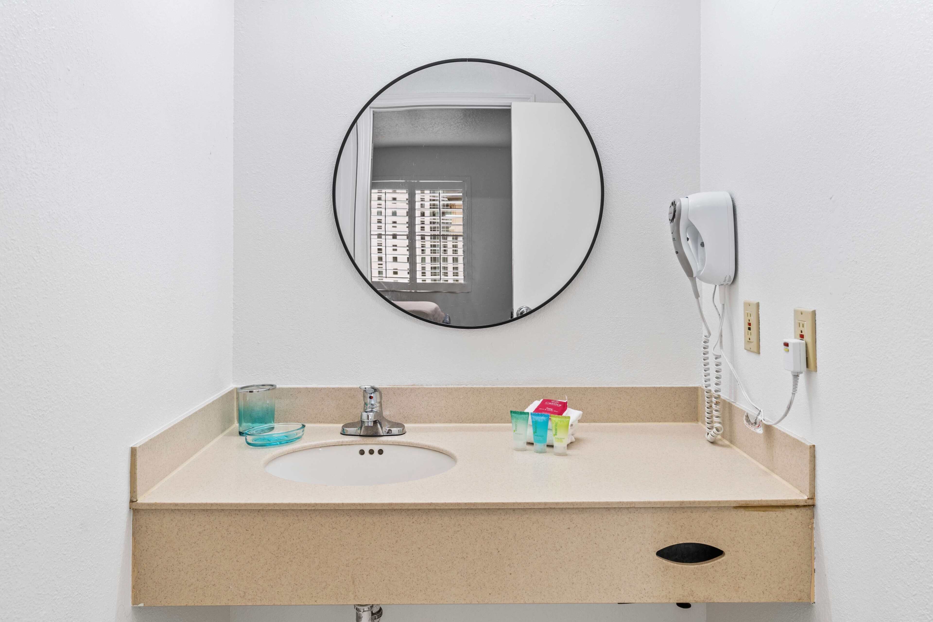 A bathroom with a sink, mirror, and a hairdryer mounted on the wall.