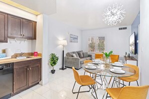 Cozinha moderna com armários de madeira escura, lava-louças e área de jantar com mesa de vidro e cadeiras amarelas.