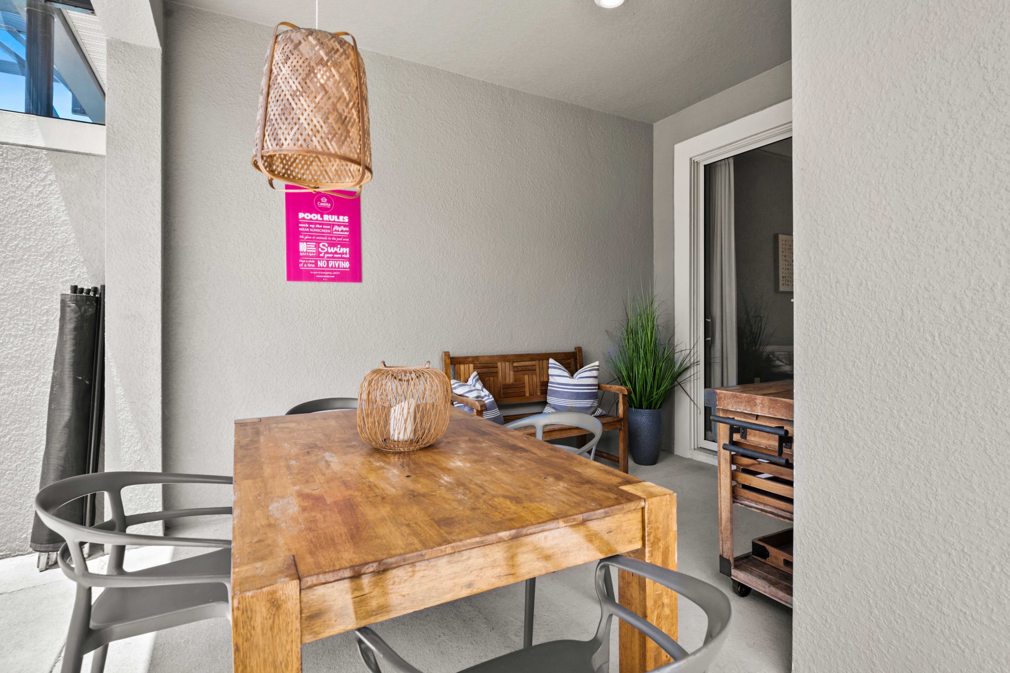 A wooden dining table with metal chairs, a wicker hanging light fixture, and a sign on the wall.