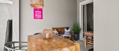 A wooden dining table with metal chairs, a wicker hanging light fixture, and a sign on the wall.