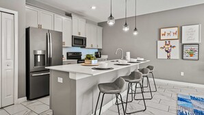 Une cuisine moderne dotée d’un îlot central, de tabourets de bar, d’appareils électroménagers en acier inoxydable et de luminaires suspendus.