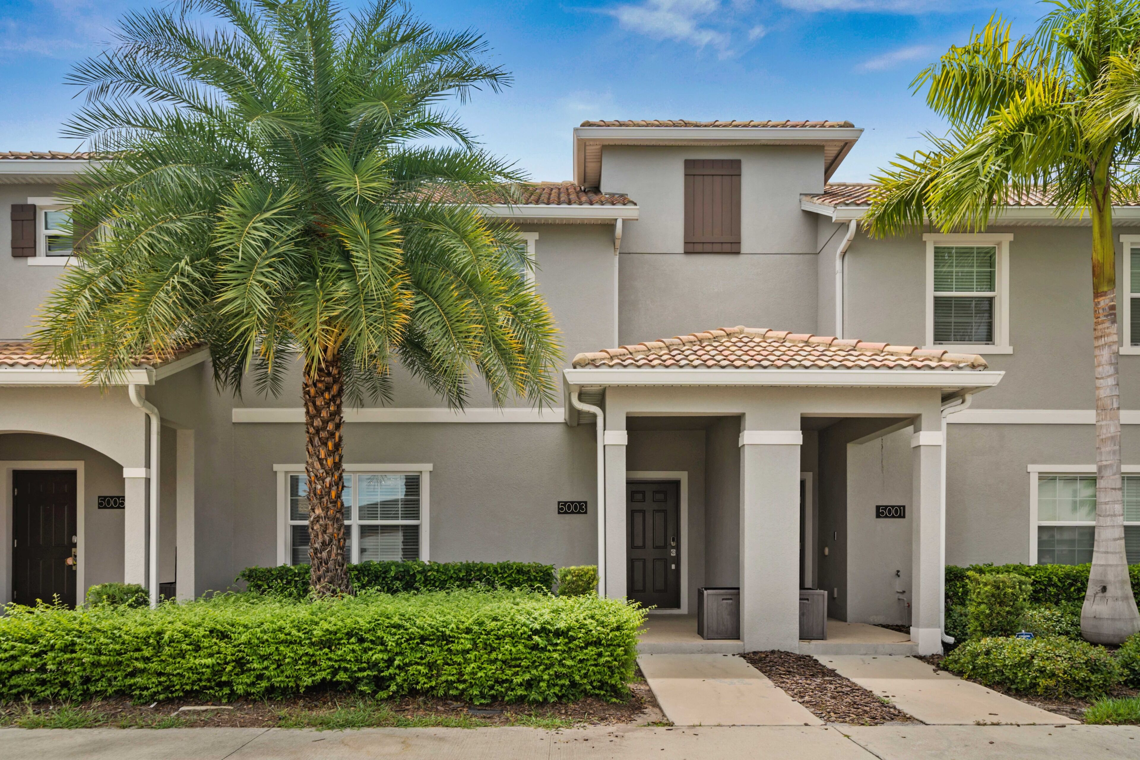 A two-story residential building with a tiled roof, a palm tree, and a well-maintained lawn.