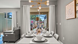 Un coin repas avec une table blanche dressée pour six personnes, des chaises grises à revêtement rembourré et un lustre moderne.