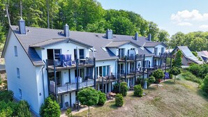 A multi-story residential building with balconies, a small garden area, and a hilly backdrop. - Residence Waldidyll FeWo Lieblingsplatz - modern vacation apartment in a quiet location (Sellin)