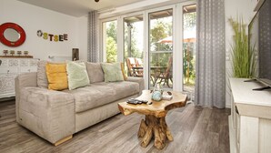 A living room with a sofa, a wooden coffee table, and a view of the outdoors through large windows. - Residence Waldidyll FeWo Lieblingsplatz - modern vacation apartment in a quiet location (Sellin)