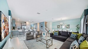 A spacious living area with a sofa, coffee table, and a dining area with chairs and a kitchen in the background. - 9046 Stinger Drive (Davenport)
