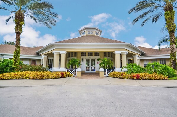 A hotel entrance with a covered porch, palm trees, and a clear sky. - 2302 Butterfly Palm Way #302 (Kissimmee)
