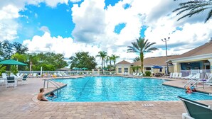 A swimming pool with lounge chairs and umbrellas, surrounded by palm trees and buildings. - 2302 Butterfly Palm Way #302 (Kissimmee)