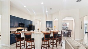 Uma cozinha ampla com armários azul escuro, uma ilha central com banquetas e uma área de jantar com uma mesa grande e cadeiras.