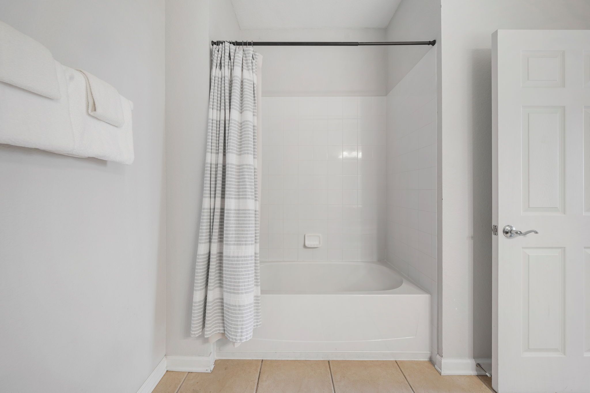 A bathroom with a shower, a bathtub, a white door, and a towel rack.
