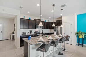 A modern kitchen with dark cabinets, a granite countertop, and a central island with bar stools. - 8918 Sydney Avenue (Kissimmee)