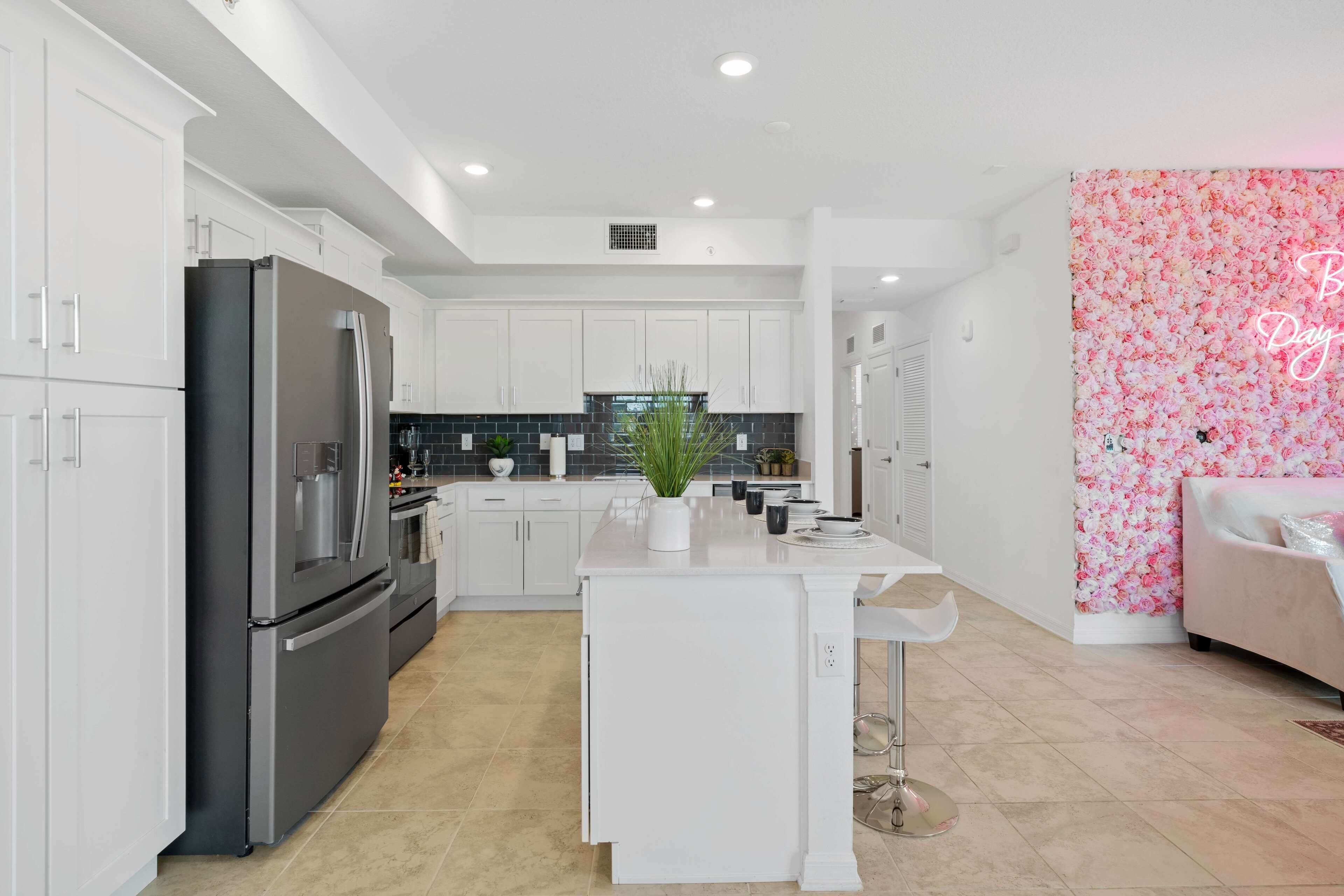 Eine moderne Küche mit weißen Schränken, einem schwarzen Kühlschrank und einer Wand mit rosa Blumenmuster.