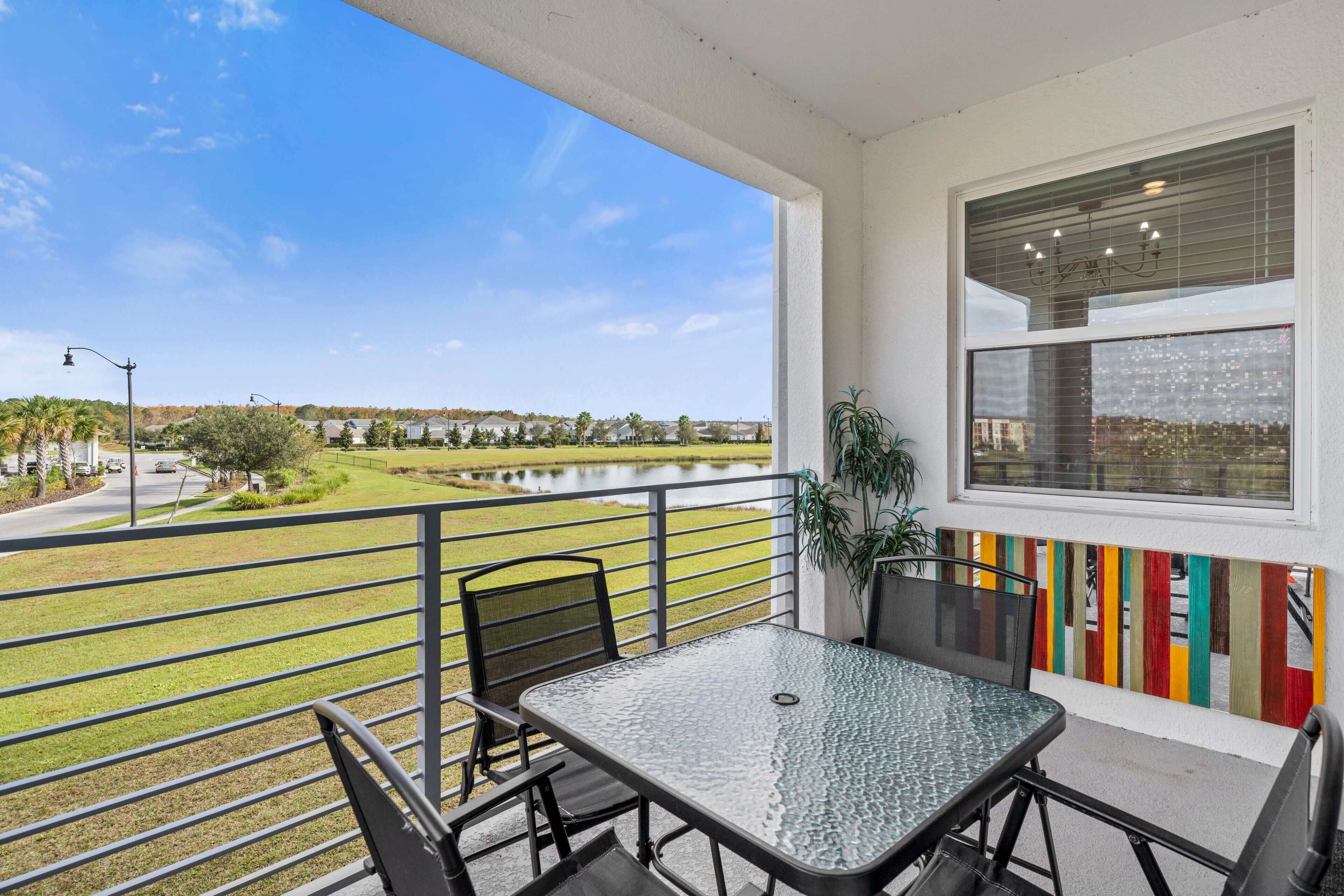 A balcony with a table and chairs, a view of a lake, and a colorful fence.