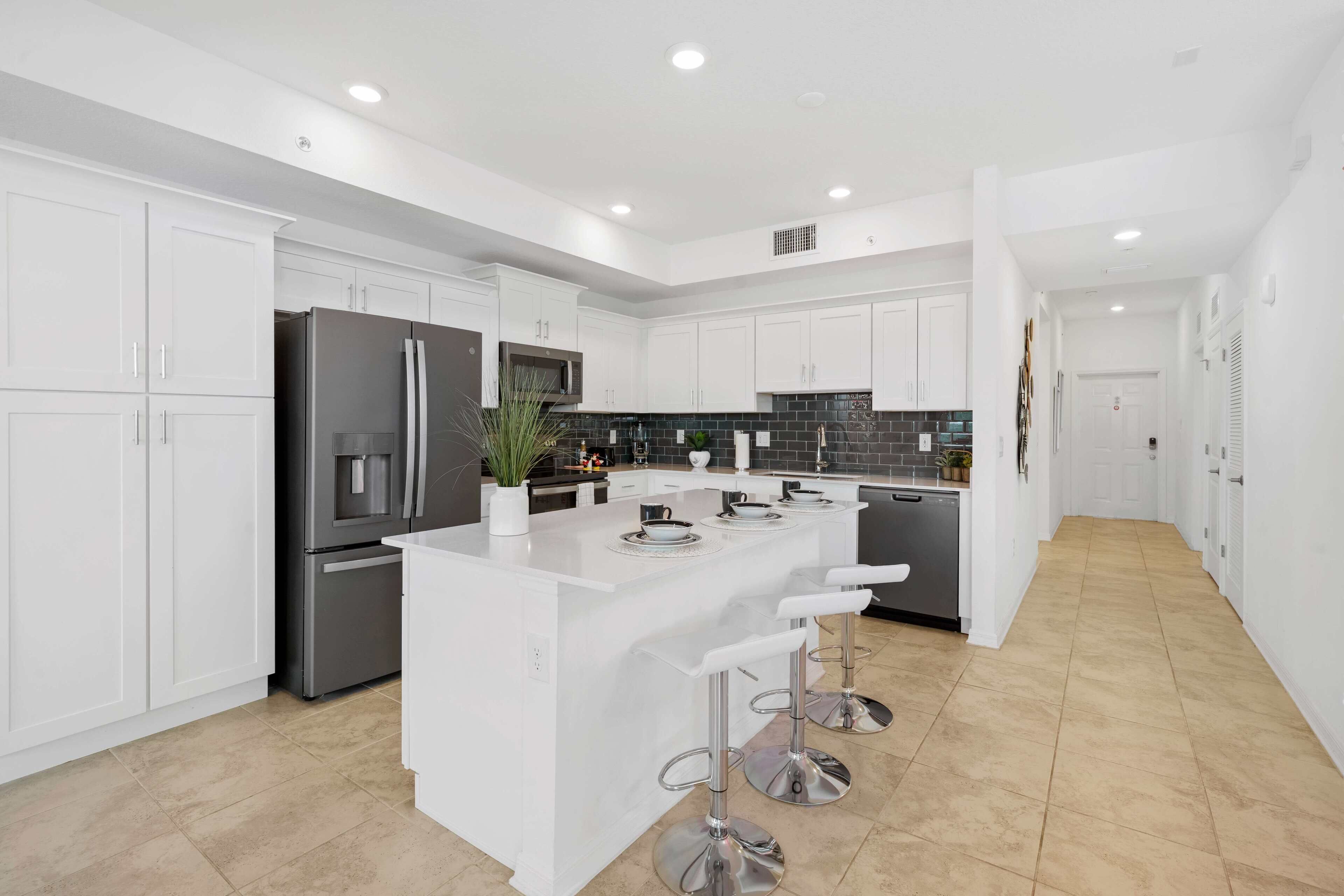 A modern kitchen with white cabinetry, stainless steel appliances, and a central island with bar stools.