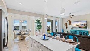 A modern kitchen with a central island, dining area with chairs, a sofa, and a TV. - 3141 Paradox Circle #406 (Kissimmee)