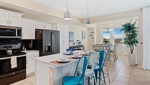 A modern kitchen with white cabinets, a black refrigerator, and a dining area with blue chairs. - 3141 Paradox Circle #406 (Kissimmee)