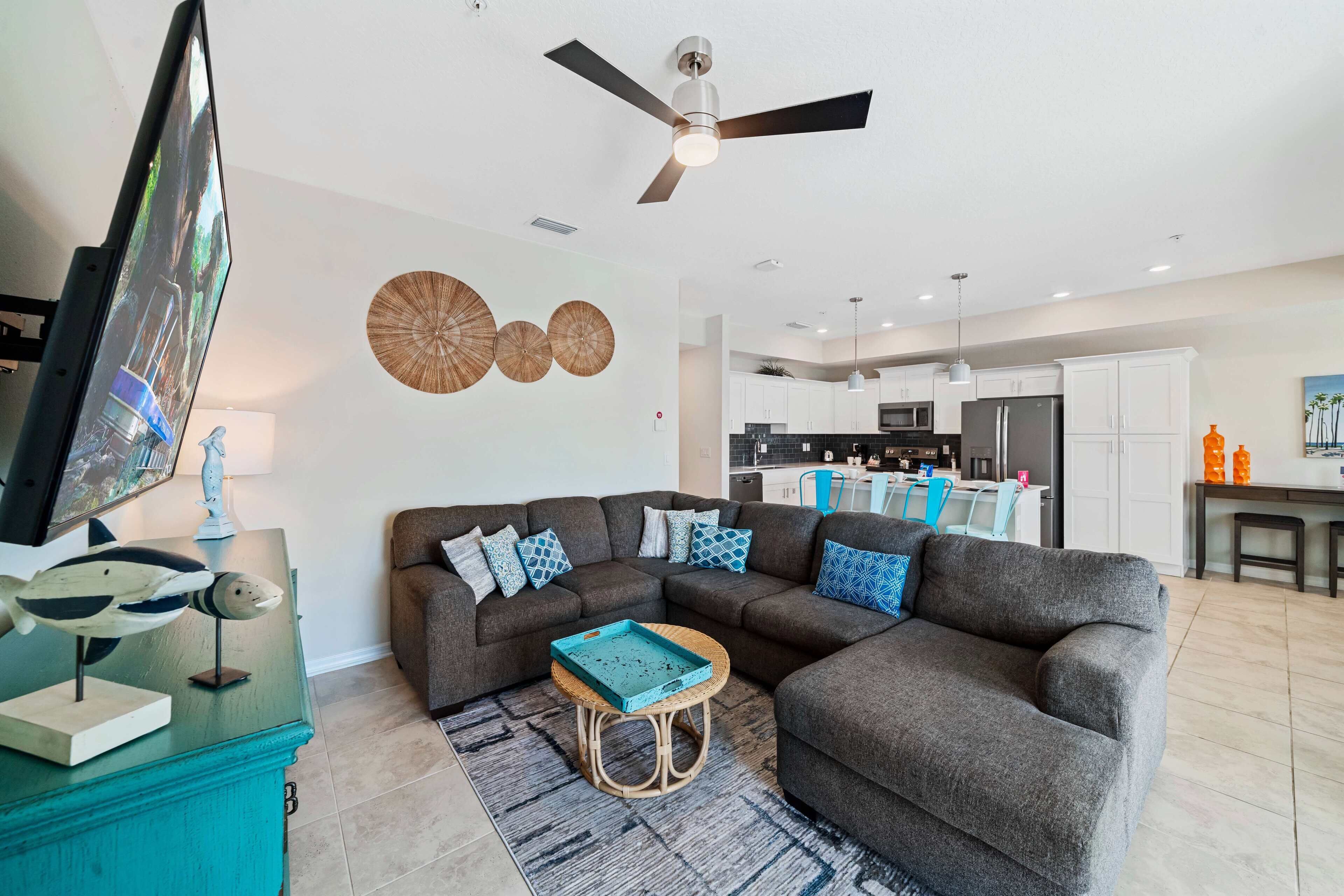 A modern living room with a sectional sofa, a flat-screen TV, and a ceiling fan.