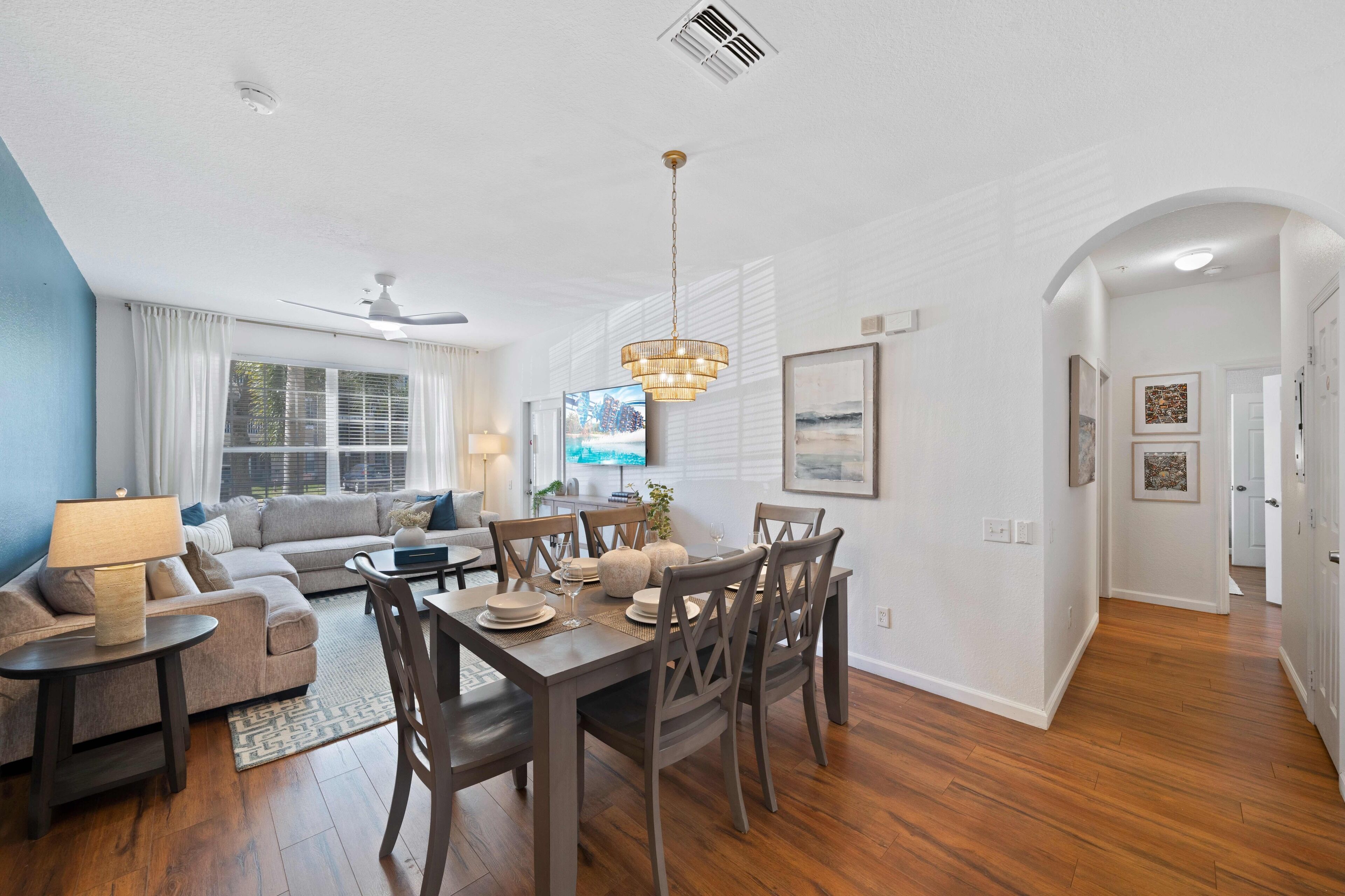 A dining area with a wooden table and chairs, a sofa, and a television in the background.