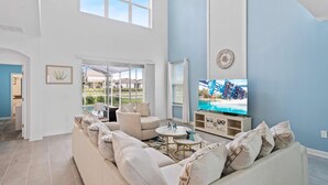 A spacious living room with a large sectional sofa, a flat-screen TV, and a view of a pool through large windows. - 520 Sticks Street (Kissimmee)