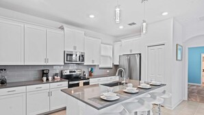 A modern kitchen with white cabinets, stainless steel appliances, and a central island with bar stools. - 520 Sticks Street (Kissimmee)