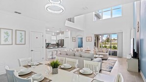 A spacious living area with a dining table set for six, a sofa, and a kitchen in the background. - 520 Sticks Street (Kissimmee)