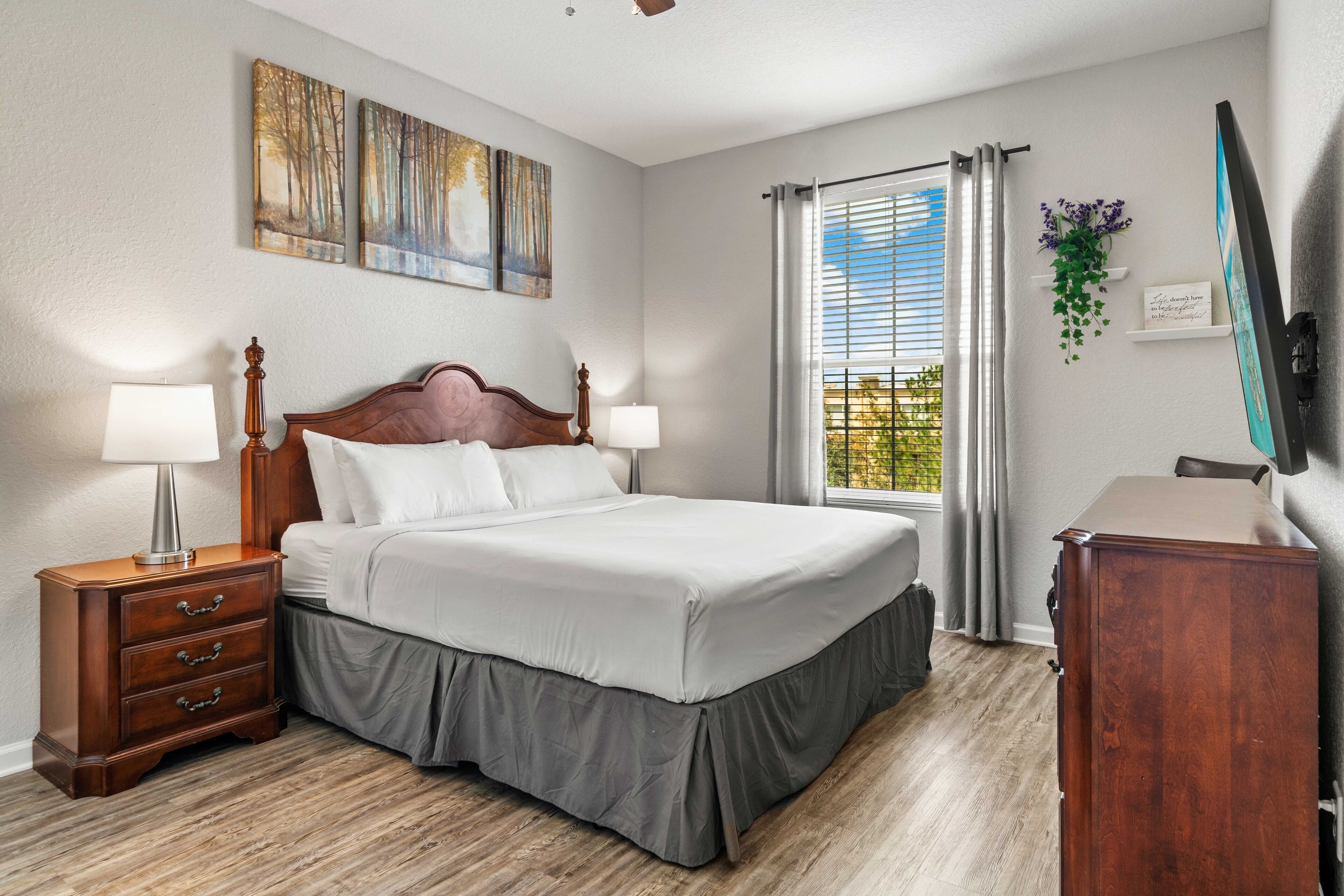 A bedroom with a large bed, two bedside tables, a dresser, and a window with curtains.