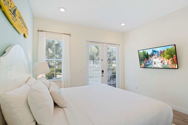 A bedroom with a large bed, a TV on the wall, and two doors with blinds. - 3050 Pirate Way (Kissimmee)
