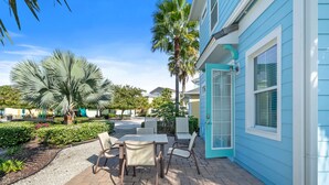 Une terrasse avec des meubles d’extérieur, des palmiers et un bâtiment dont le revêtement extérieur est bleu.