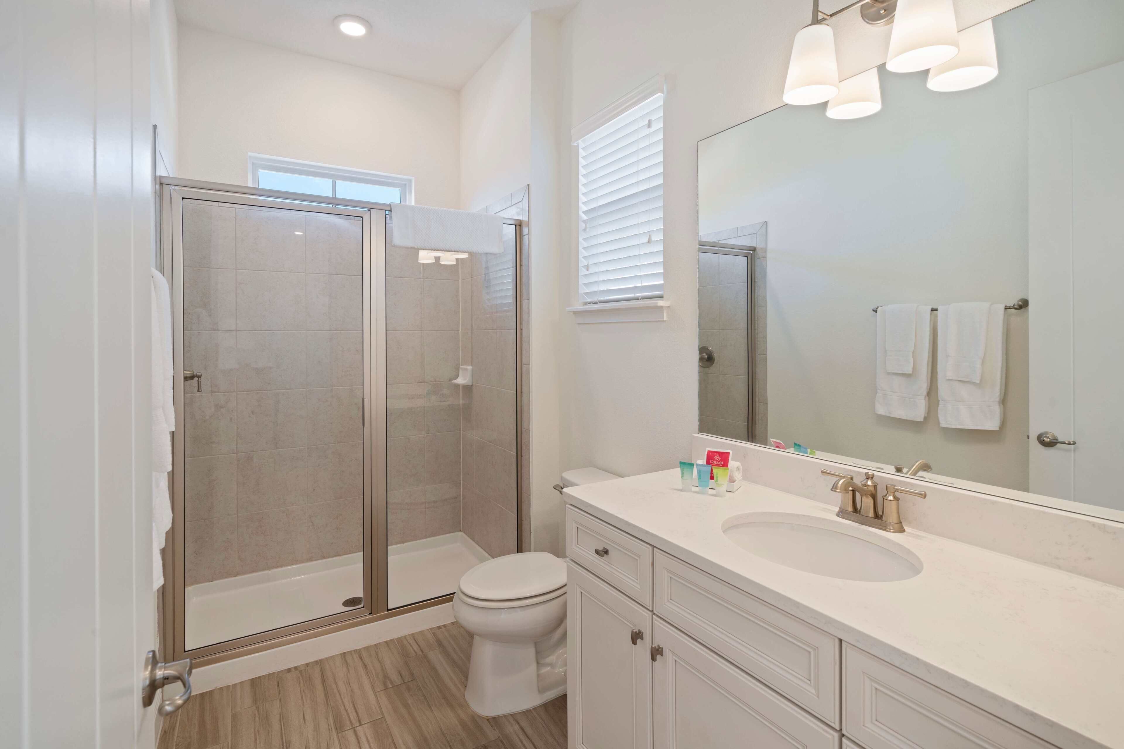 A modern bathroom with a glass-enclosed shower, a white sink, and a large mirror.