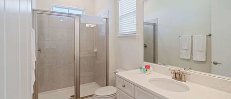 A modern bathroom with a glass-enclosed shower, a white sink, and a large mirror.