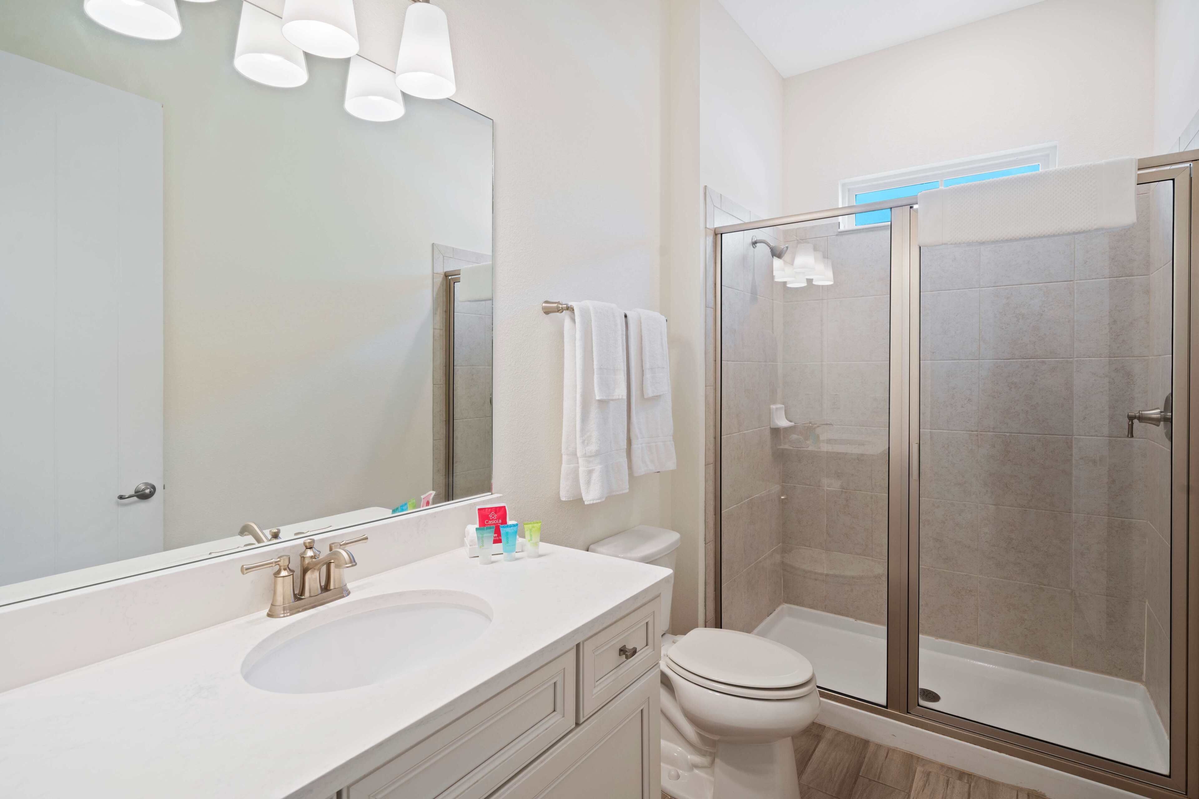 Un baño moderno con un espejo grande, lavamanos blanco y cabina de ducha con mampara de vidrio.
