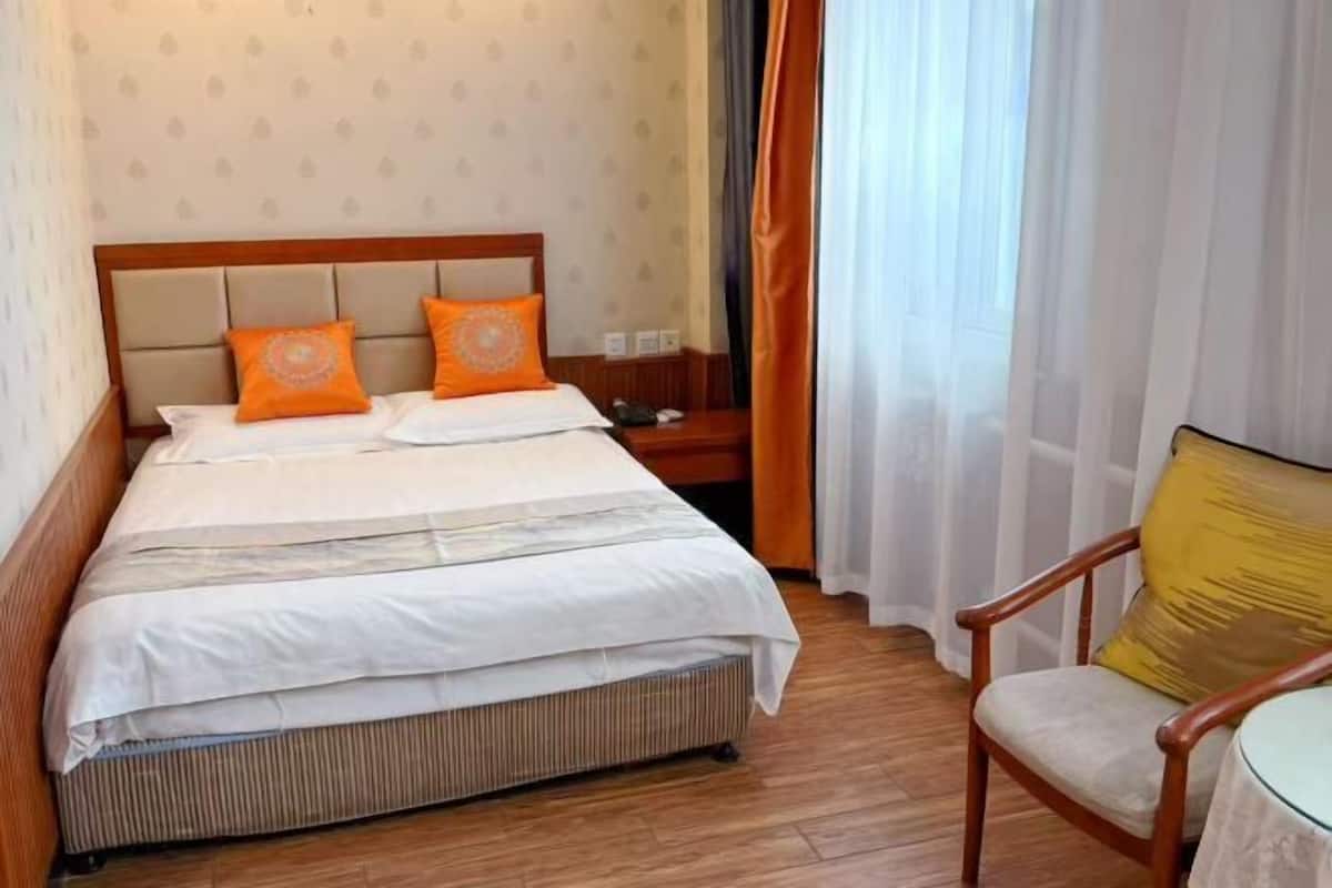 A hotel room with a bed, a nightstand, a chair, and a window with curtains.