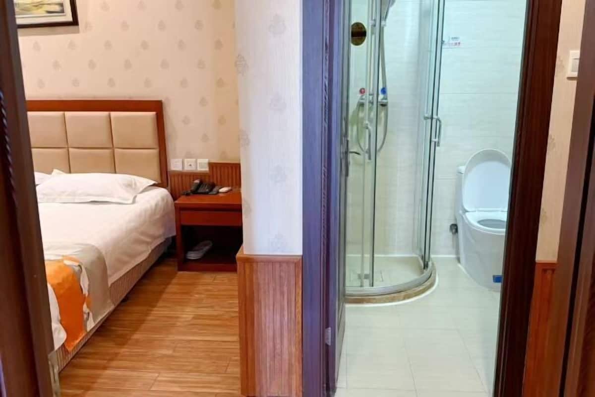 A hotel room with a bed, a bedside table, a shower enclosure, and a toilet.